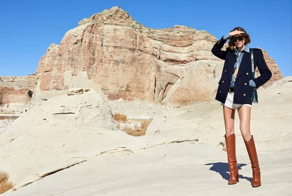 It seems like you may have meant to type "shorter." Here's a more concise version of the description:
A model in a tailored Yves Saint Laurent blazer and knee-high boots poses in a rocky desert setting.