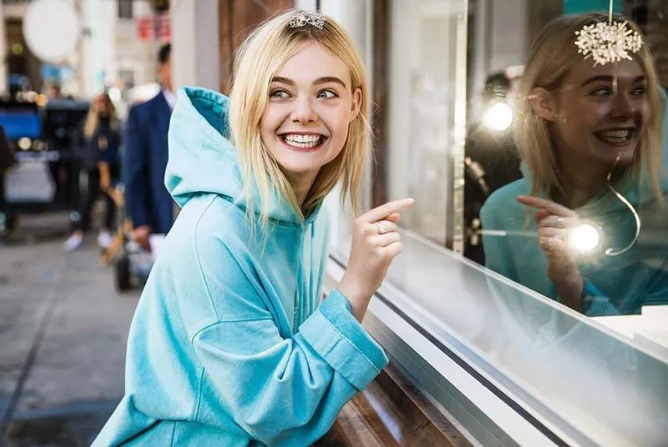 A smiling model in a blue hoodie admires jewelry in a Tiffany & Co. window display.